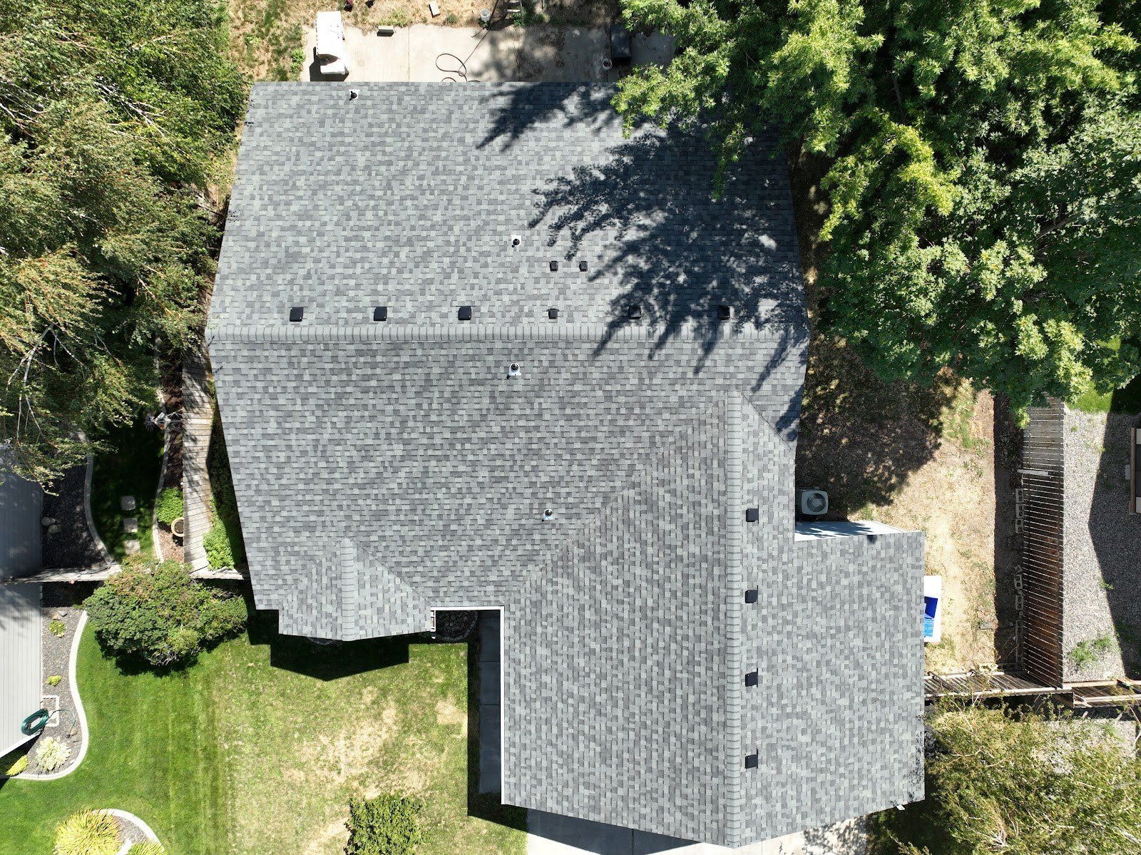 Aerial view of a finished gray architectural shingle roof over a shaded yard