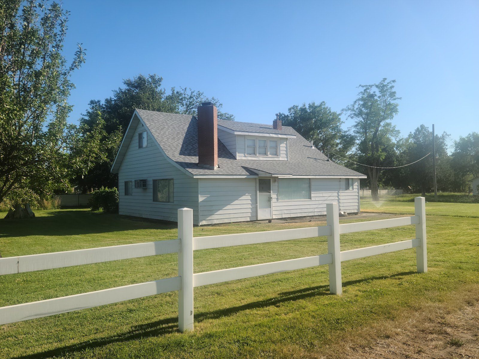 Two-story farmhouse with a new roof behind a white rail fence